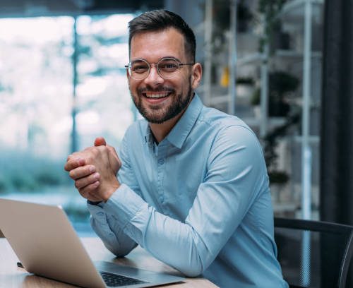 Shot of a businessman sitting on desk in modern office and working on laptop. Elegant handsome businessman sitting in his office and using laptop.