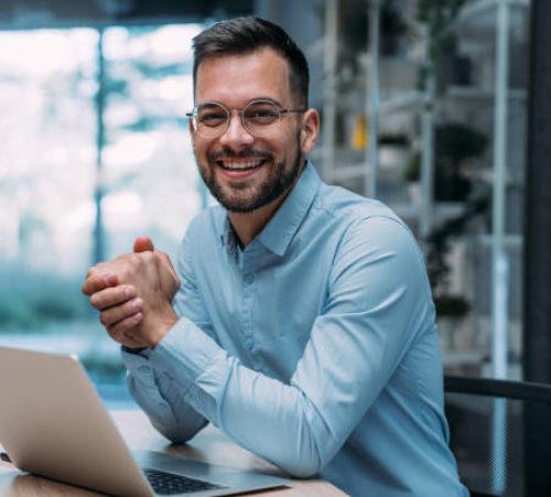 Shot of a businessman sitting on desk in modern office and working on laptop. Elegant handsome businessman sitting in his office and using laptop.